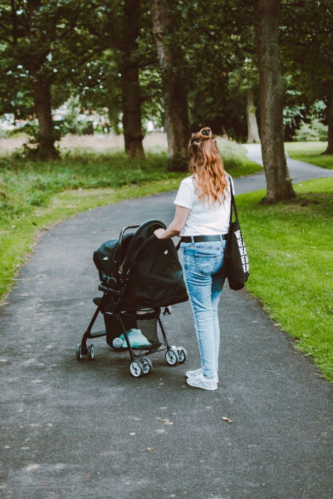 Vrouw wandelt met een kinderwagen over een groen parkpad